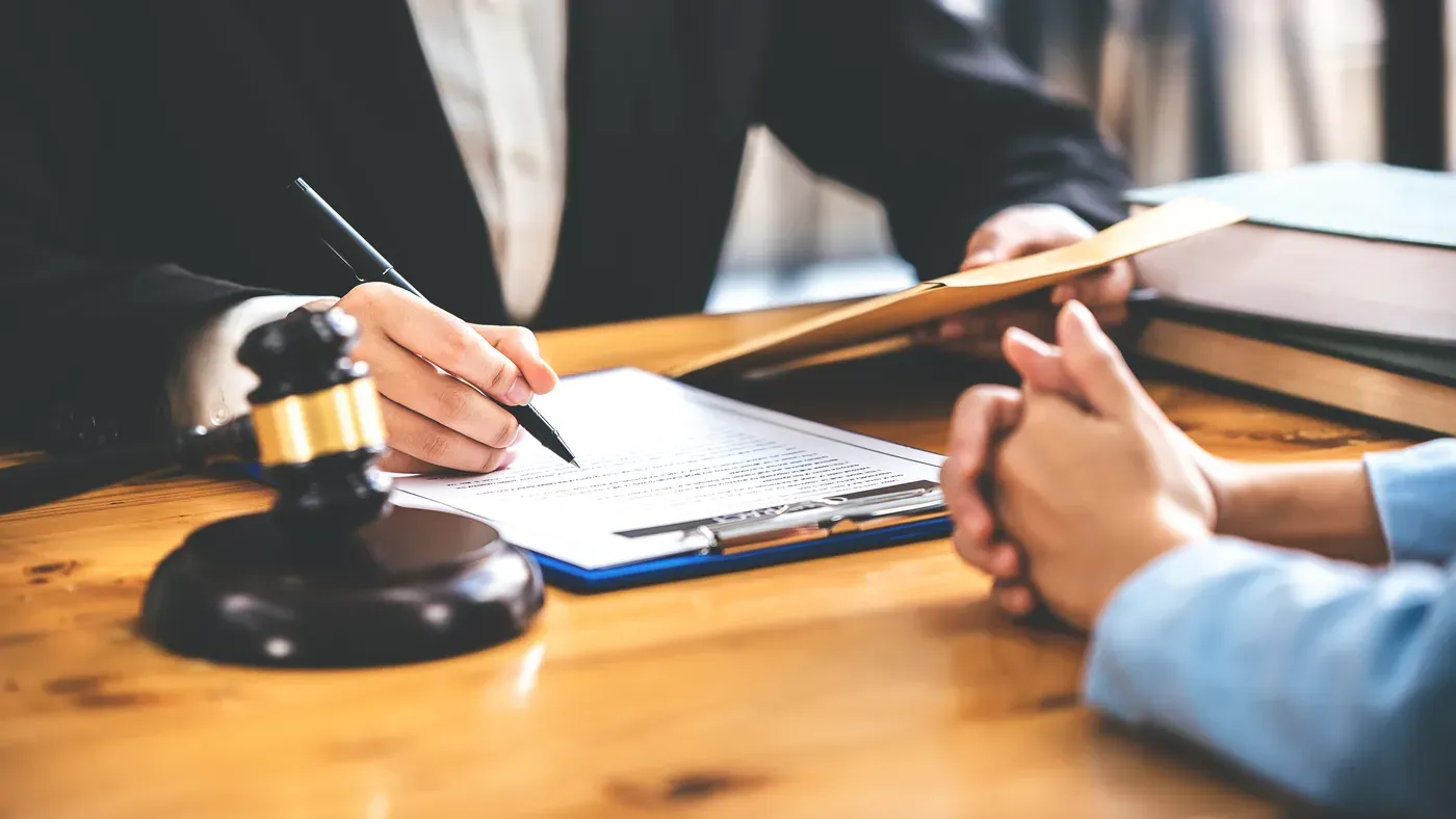 A client signing paperwork across a desk while an attorney guides them