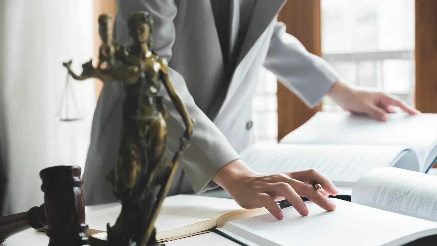 A statue of the scales of justice on a desk beside a gavel and open law books