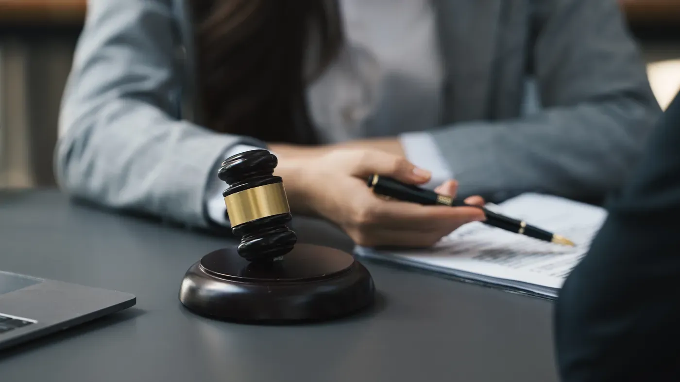 A wooden gavel on a desk while two people review documents across the table