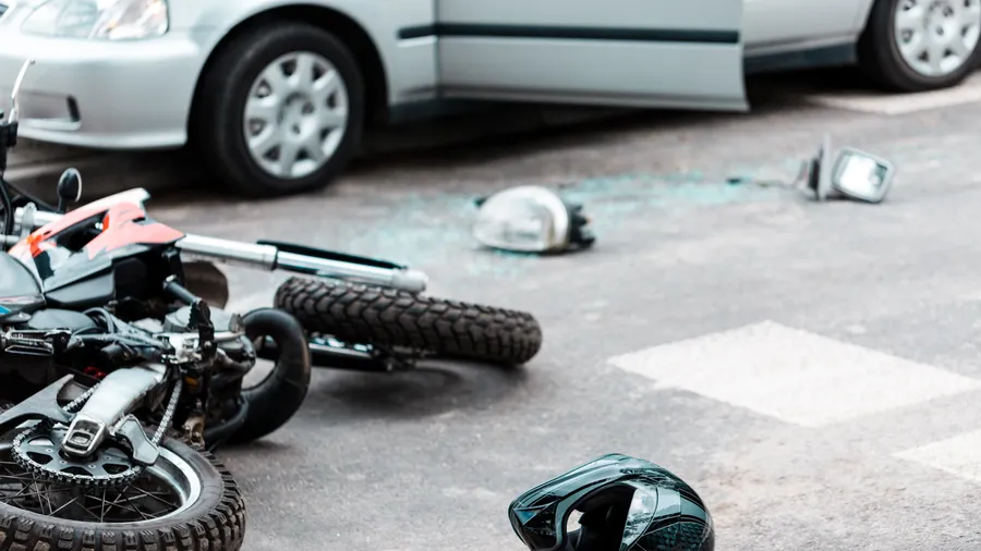 A motorcycle down in the road beside a car after a collision, helmet in the foreground