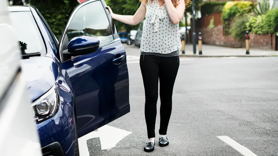 A shaken driver standing beside her car at a street crossing after a collision