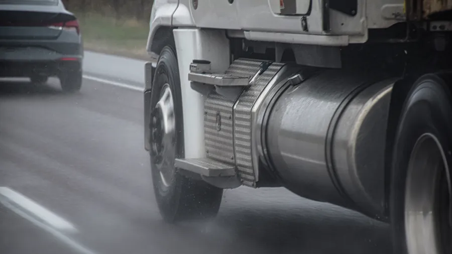 A semi truck traveling on a wet highway beside a passenger car
