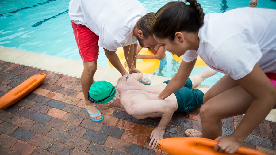 Two responders assisting a man on a wet pool deck