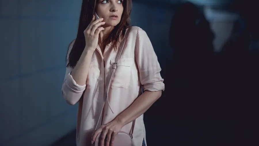 A woman alone at night on her phone in a dim walkway