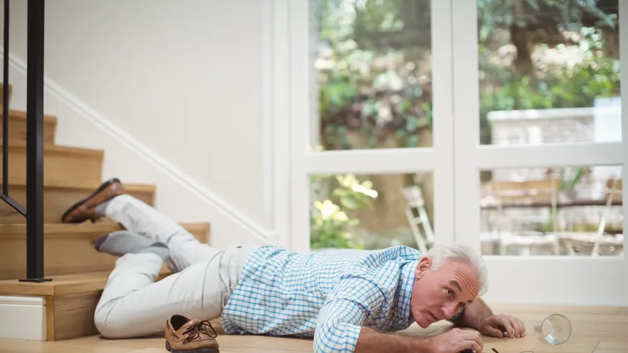 An older man on the floor at the foot of a staircase after a fall