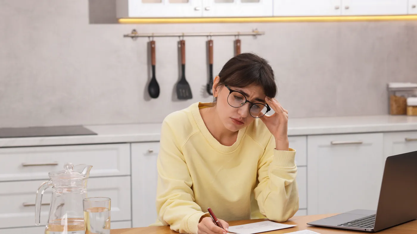 A person at a kitchen table working through a stack of paperwork